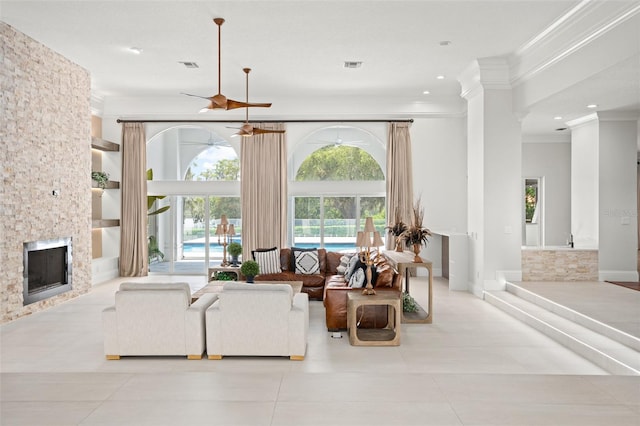 living room with crown molding, light tile patterned flooring, a stone fireplace, and ornate columns