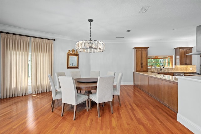 dining space with light wood-type flooring, sink, crown molding, and a chandelier