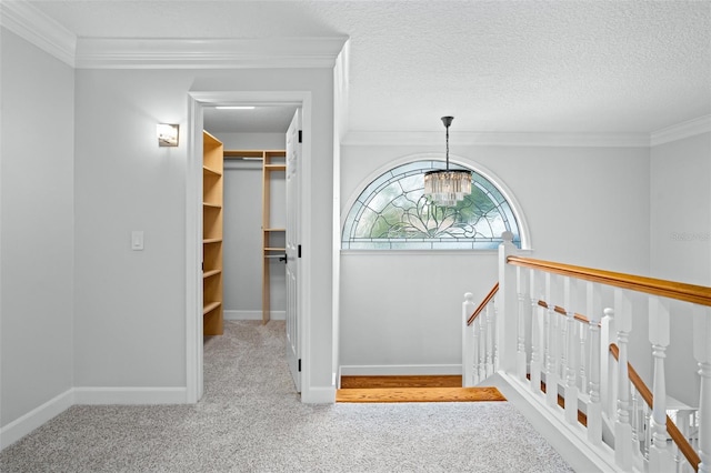 hall with an inviting chandelier, a textured ceiling, carpet floors, and ornamental molding