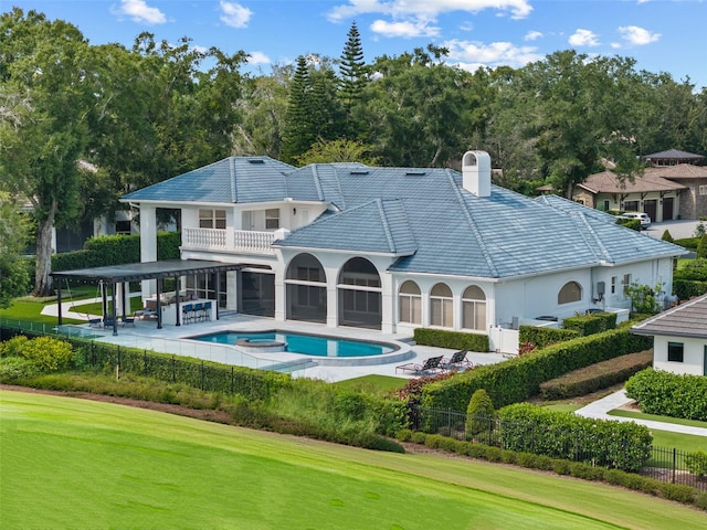 rear view of property featuring a balcony, a swimming pool with hot tub, a patio, and a lawn