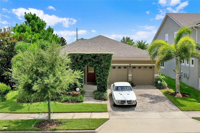 view of front of property featuring an attached garage, roof with shingles, decorative driveway, stucco siding, and a front yard