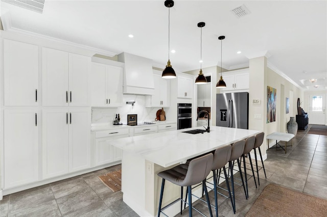 kitchen featuring white cabinets, custom range hood, appliances with stainless steel finishes, a kitchen breakfast bar, and a kitchen island with sink