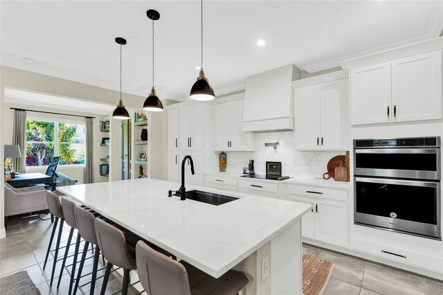 kitchen with pendant lighting, a center island with sink, custom exhaust hood, a sink, and light stone countertops