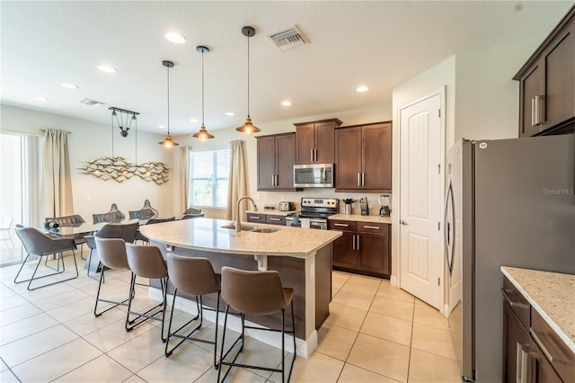 kitchen with sink, decorative light fixtures, appliances with stainless steel finishes, light stone counters, and a center island with sink