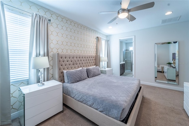 bedroom with ceiling fan, light colored carpet, ensuite bathroom, and multiple windows