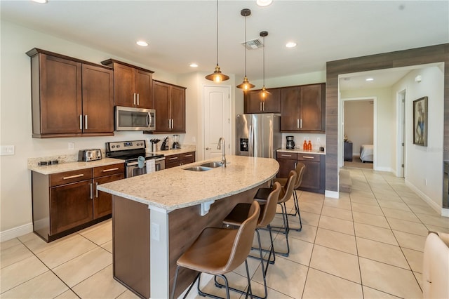 kitchen with stainless steel appliances, decorative light fixtures, sink, light stone countertops, and a breakfast bar