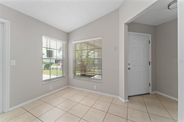 foyer entrance with lofted ceiling, a textured ceiling, baseboards, and light tile patterned floors