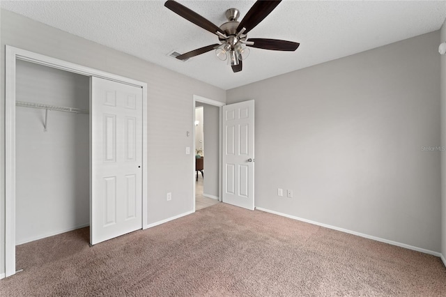 unfurnished bedroom with a closet, dark carpet, ceiling fan, a textured ceiling, and baseboards