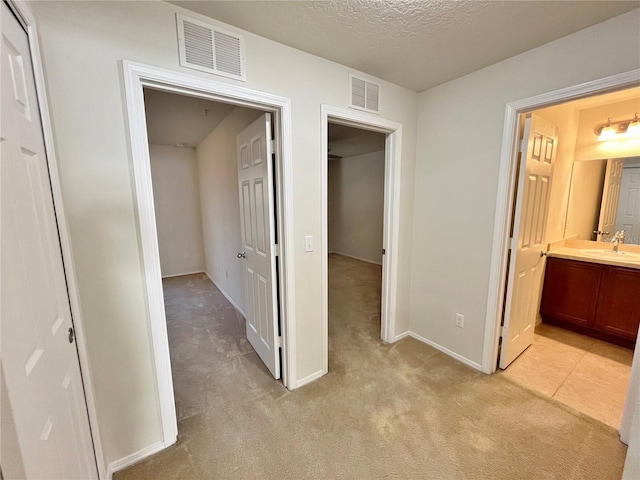 hall with light carpet, a textured ceiling, and sink