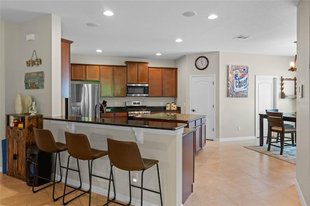 kitchen with a center island with sink, stainless steel appliances, sink, light tile patterned floors, and a breakfast bar area