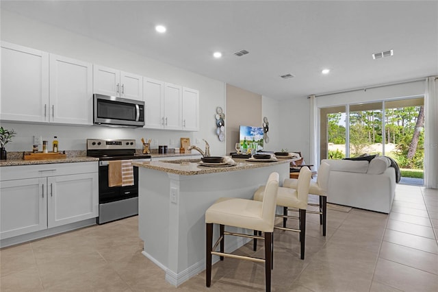 kitchen featuring stainless steel appliances, light stone countertops, a kitchen island with sink, white cabinets, and light tile patterned floors