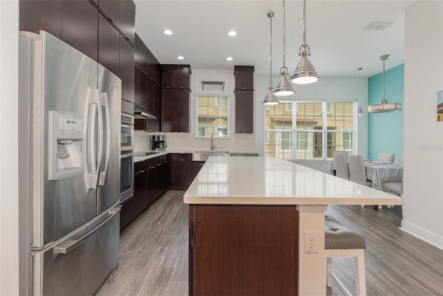 kitchen with light countertops, pendant lighting, a center island, a healthy amount of sunlight, and stainless steel refrigerator with ice dispenser