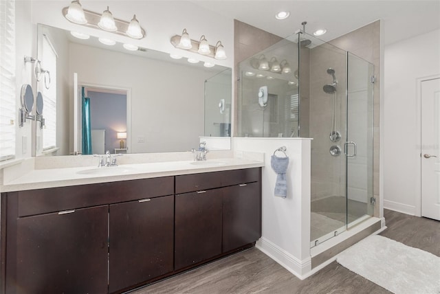 bathroom featuring a sink, double vanity, wood finished floors, and a stall shower