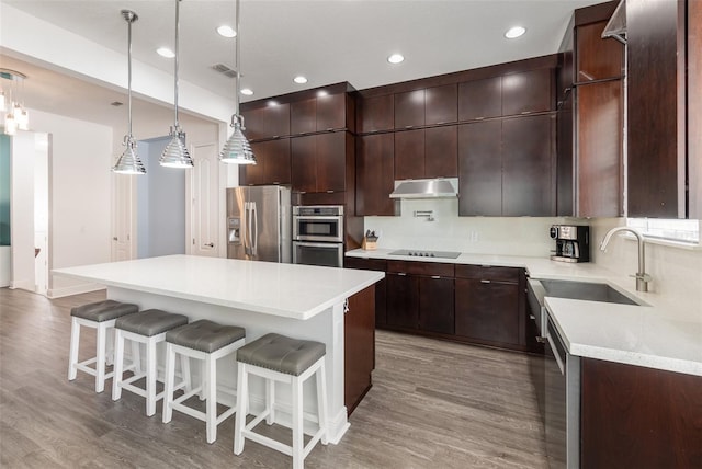 kitchen featuring under cabinet range hood, stainless steel appliances, light countertops, a center island, and pendant lighting