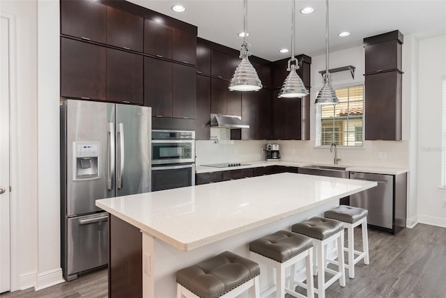 kitchen featuring under cabinet range hood, stainless steel appliances, a kitchen breakfast bar, hanging light fixtures, and a center island