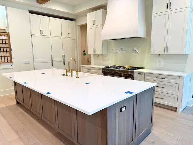 kitchen with a spacious island, sink, double oven range, custom range hood, and white cabinets