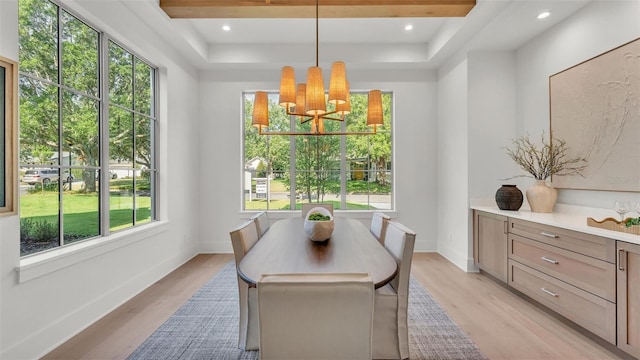 dining room with light wood-type flooring, an inviting chandelier, a tray ceiling, and plenty of natural light