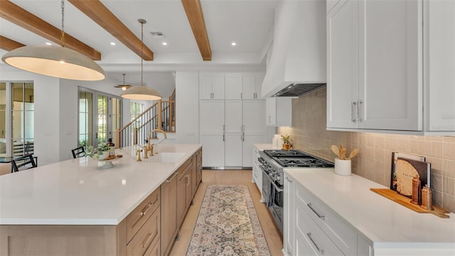kitchen with beamed ceiling, a sink, decorative backsplash, custom range hood, and range with two ovens