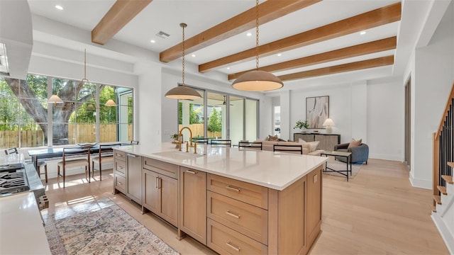 kitchen with a sink, beam ceiling, light countertops, visible vents, and pendant lighting