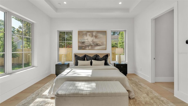 bedroom featuring recessed lighting, light wood-style flooring, a raised ceiling, and baseboards