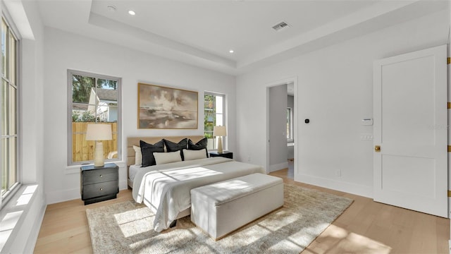 bedroom featuring a raised ceiling, light wood-type flooring, visible vents, and multiple windows
