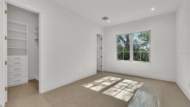 unfurnished bedroom featuring a walk in closet, carpet flooring, baseboards, and visible vents
