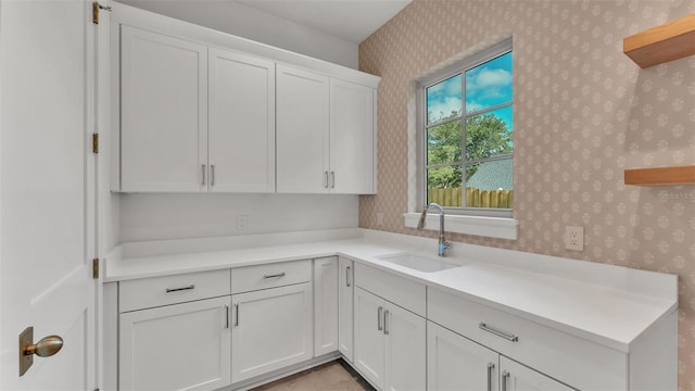 kitchen with white cabinetry, wallpapered walls, light countertops, and a sink