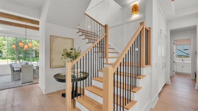 stairway with a chandelier, beam ceiling, wood finished floors, and baseboards