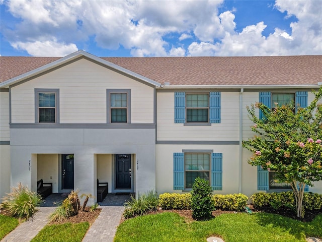 multi unit property featuring a front yard, roof with shingles, and stucco siding