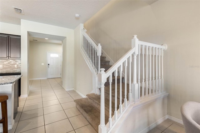 staircase featuring baseboards, a textured ceiling, visible vents, and tile patterned floors