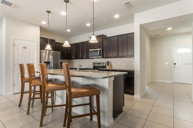 kitchen featuring tasteful backsplash, appliances with stainless steel finishes, light stone countertops, a breakfast bar area, and a center island with sink