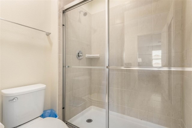 bathroom featuring a shower with shower door and toilet