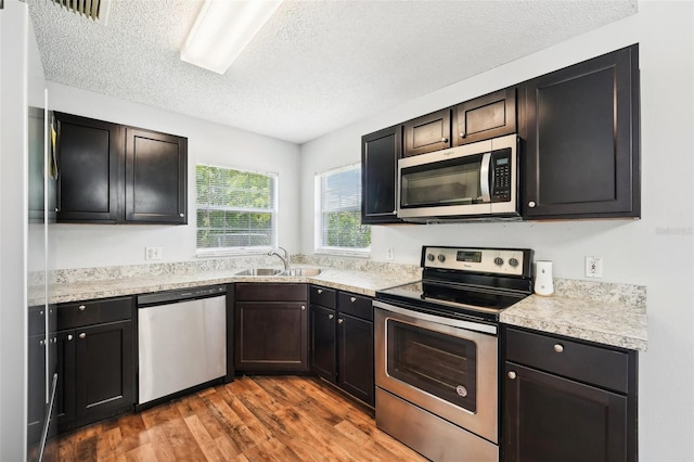 kitchen featuring appliances with stainless steel finishes, a textured ceiling, wood-type flooring, and sink