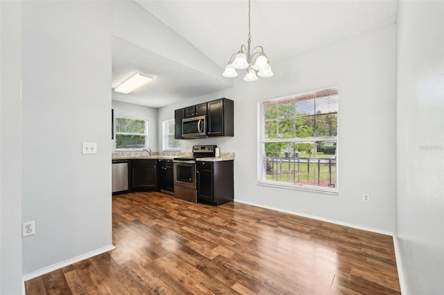 kitchen featuring a notable chandelier, vaulted ceiling, light stone counters, dark wood-type flooring, and appliances with stainless steel finishes