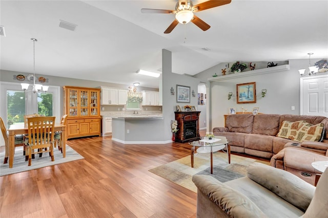 living room with light hardwood / wood-style flooring, ceiling fan with notable chandelier, and vaulted ceiling