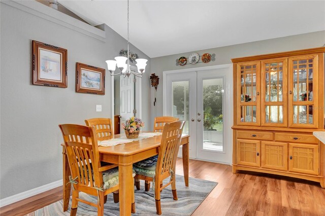 dining room with french doors, light hardwood / wood-style floors, a chandelier, and vaulted ceiling