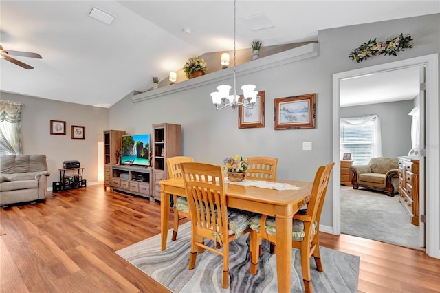 dining space with ceiling fan with notable chandelier, lofted ceiling, and light hardwood / wood-style flooring