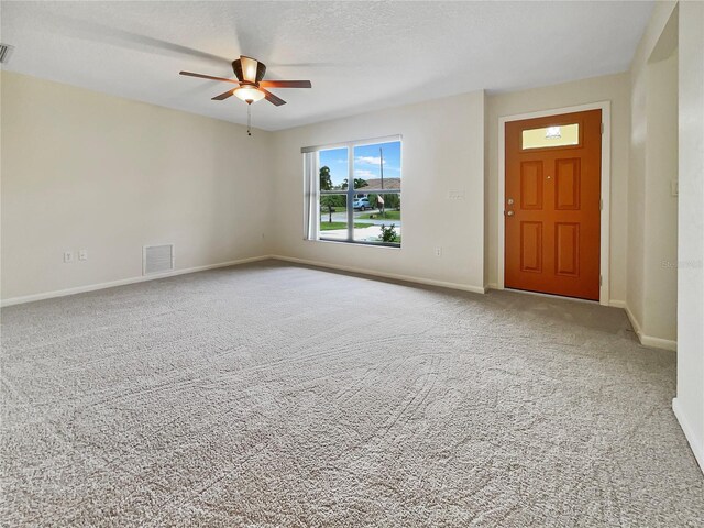 carpeted foyer entrance featuring a textured ceiling, ceiling fan, visible vents, and baseboards