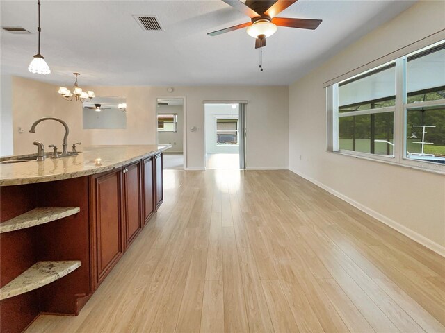 kitchen with light stone counters, decorative light fixtures, visible vents, a sink, and light wood-type flooring