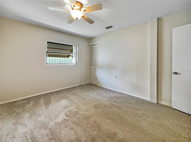 carpeted spare room with a textured ceiling, ceiling fan, visible vents, and baseboards