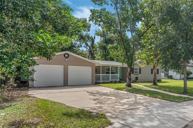 ranch-style home with a garage, a front lawn, a porch, and central AC unit