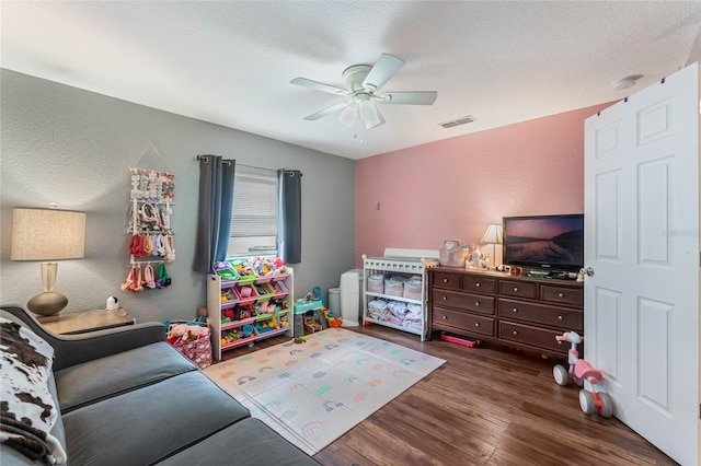 playroom with ceiling fan, visible vents, a textured wall, and wood finished floors