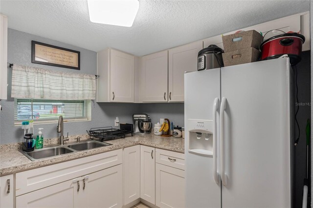 kitchen with white fridge with ice dispenser, white cabinetry, a textured ceiling, and sink