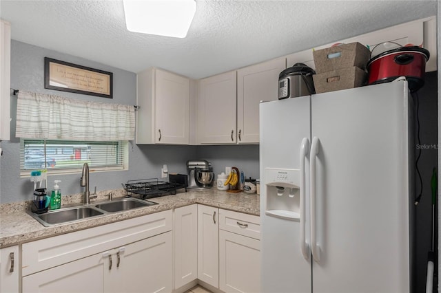 kitchen with a textured ceiling, white refrigerator with ice dispenser, light countertops, and a sink