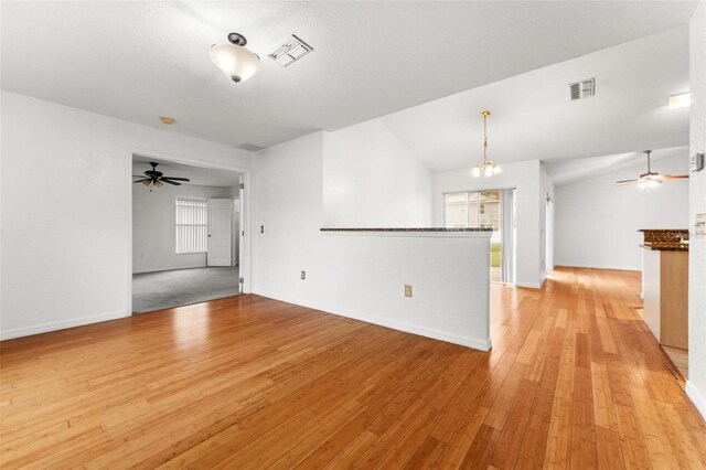 unfurnished living room with ceiling fan with notable chandelier, vaulted ceiling, and light colored carpet