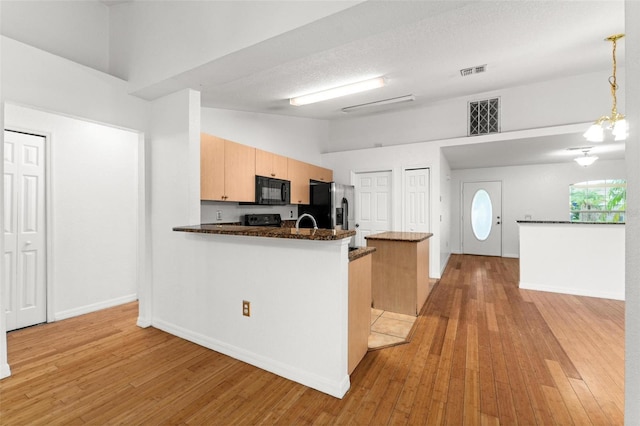 kitchen featuring light hardwood / wood-style flooring, hanging light fixtures, vaulted ceiling, kitchen peninsula, and stainless steel fridge