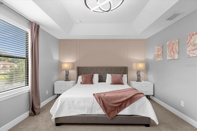 bedroom with light carpet and a tray ceiling