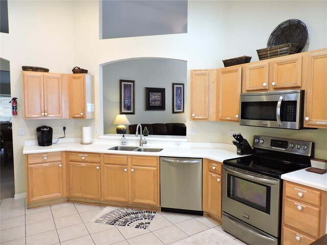 kitchen featuring sink, appliances with stainless steel finishes, light brown cabinetry, a towering ceiling, and light tile patterned floors