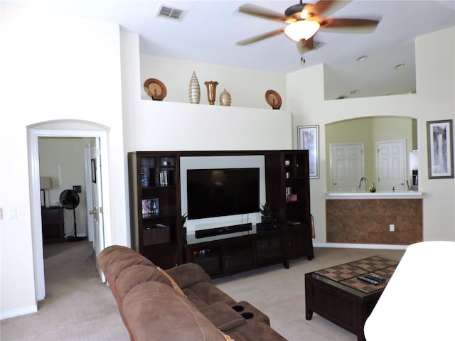 living area with arched walkways, visible vents, ceiling fan, and light carpet