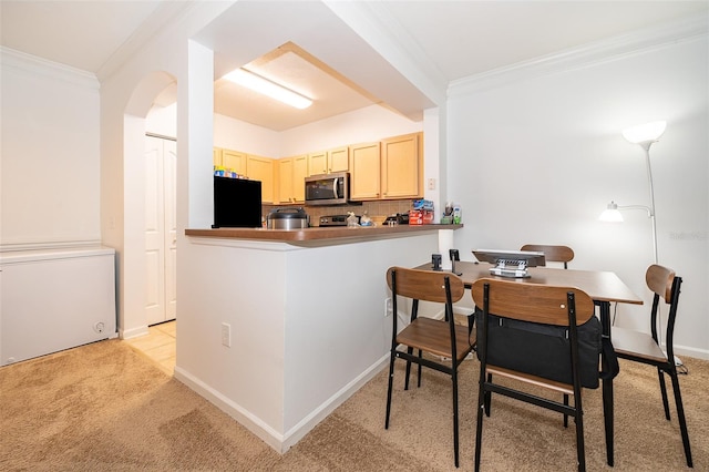 kitchen featuring black refrigerator, light colored carpet, kitchen peninsula, and crown molding